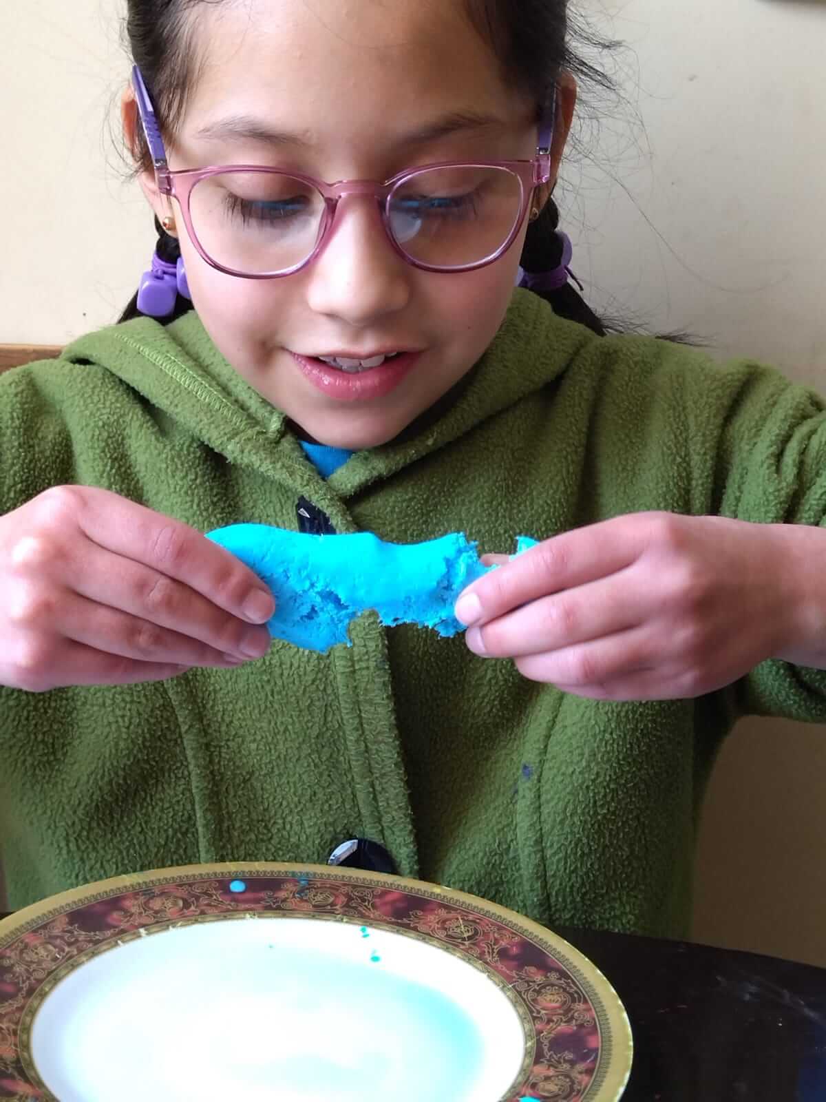 Niña con lentes rosados modelando masa azul durante la actividad de manualidades del taller