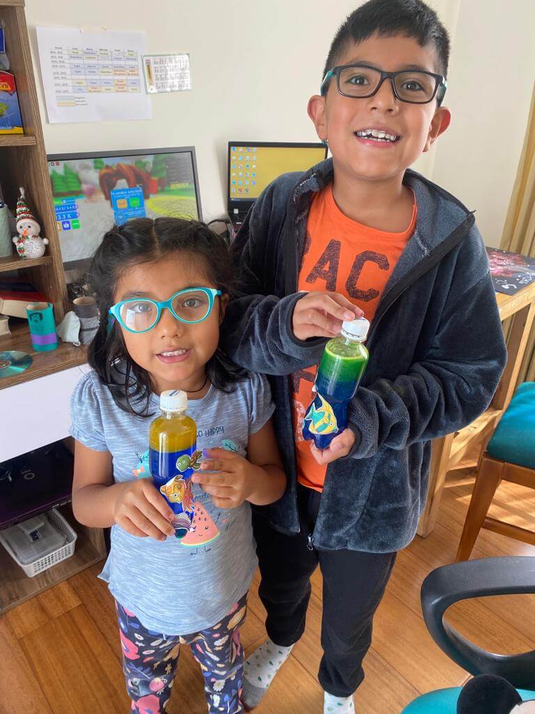 Dos niños mostrando sus botellas sensoriales decoradas con líquido de colores, creadas con material reciclado