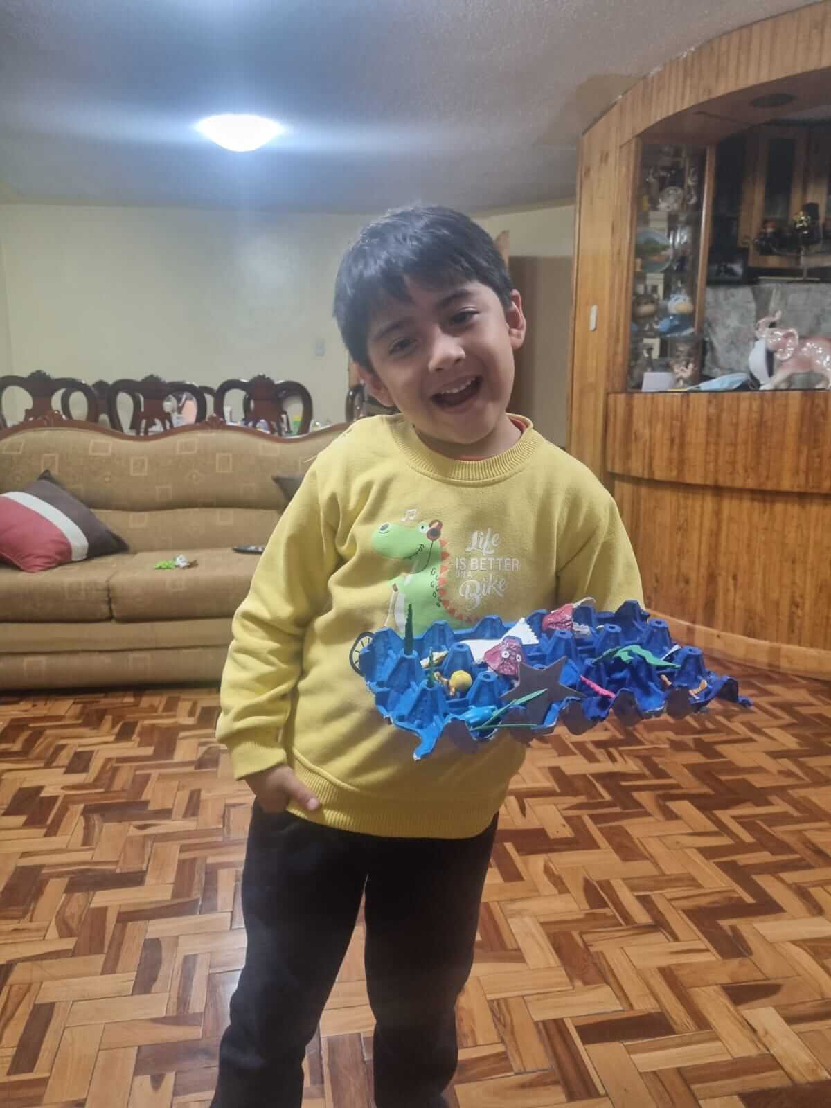 Niño feliz sosteniendo su diorama submarino hecho con cartón de huevos azul y figuras de animales marinos